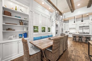 A kitchen with white cabinetry, a wooden dining table, wicker chairs, and a blue patterned bench.