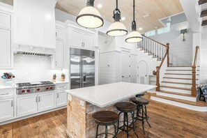 A kitchen with white cabinetry, a marble countertop, stainless steel appliances, and a wooden staircase.