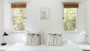 A bedroom with a large bed, two windows with blinds, a bedside table with a lamp, and a framed picture on the wall. - Silver Lake Mid-century Nestled in the Treetops (Los Angeles)