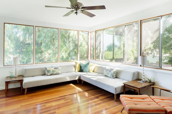 A room with a large window, a ceiling fan, and a wooden floor. - Silver Lake Mid-century Nestled in the Treetops (Los Angeles)