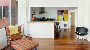 A modern living room with a striped sofa, a black chair, and a kitchen area with a painting on the wall. - Silver Lake Mid-century Nestled in the Treetops (Los Angeles)