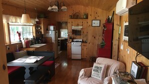 A cozy cabin interior with wooden walls, a dining area with benches, a kitchen with a stove and refrigerator, and a living area with a sofa and a sign reading "Farmers Market". - Charming Santa Ynez farmhouse (Santa Ynez)