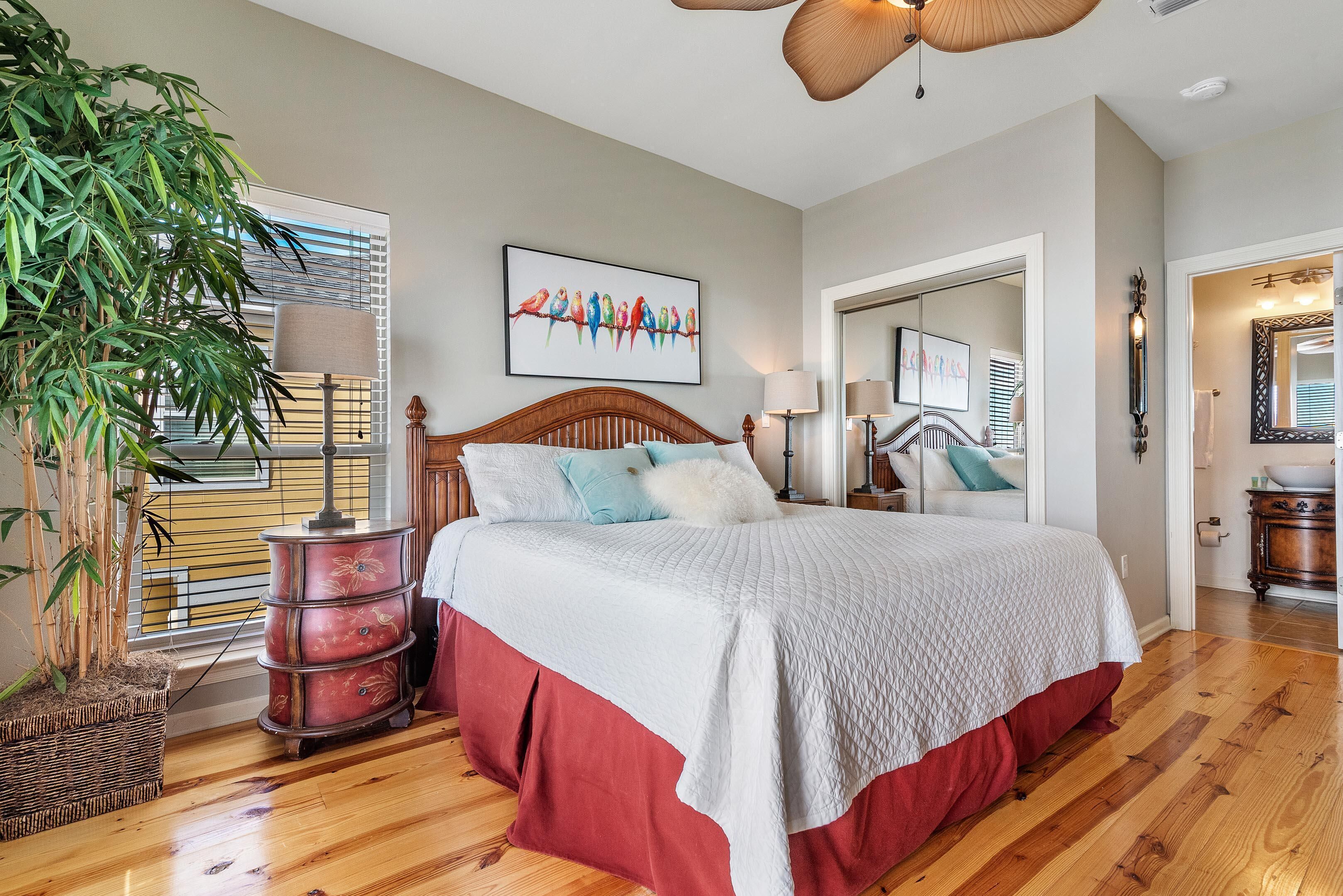 A bedroom with a wooden bed, a large window, a potted plant, and a mirror.