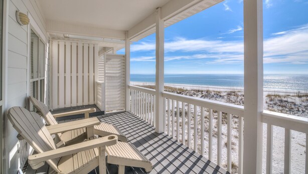 A covered porch with two Adirondack chairs, a view of the beach, and a white railing.