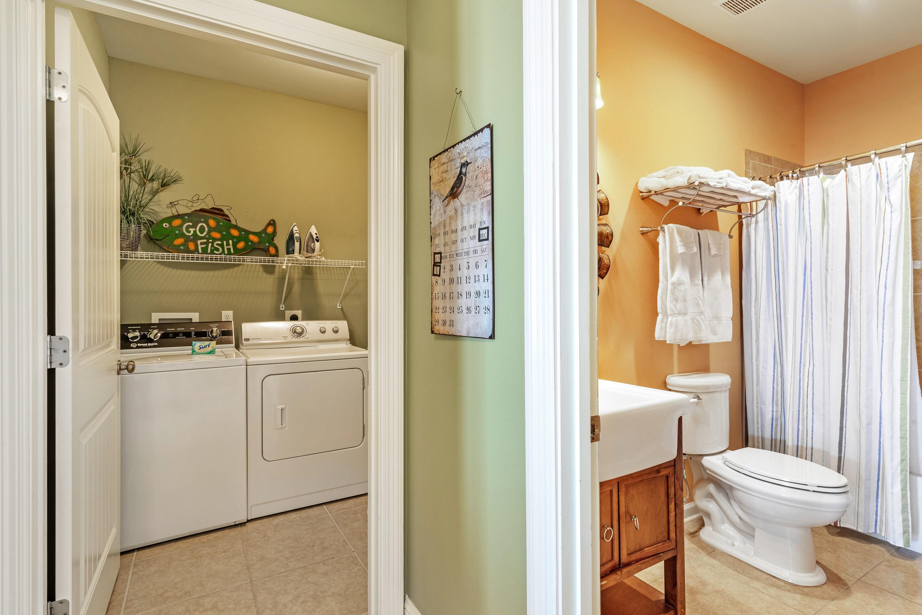 A laundry room with a washing machine and dryer, a calendar on the wall, and a shelf with decorative items.