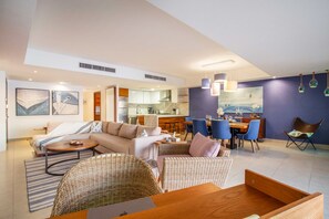 A modern living room with a sofa, coffee table, and wicker chairs. There is a dining area with a table and chairs. The kitchen is visible in the background. - Luxurious, Beachfront 2bed/2 bath Condo with Designer Finishes (Puerto Vallarta)