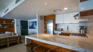 Une cuisine moderne dotée d’un plan de travail en marbre, de tabourets de bar en bois et d’appareils électroménagers en acier inoxydable.