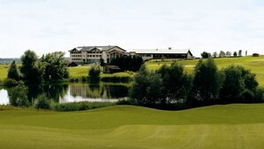A golf course with a pond, a clubhouse, and a large building in the background. - Hostellerie Du Chambellan (Pontpierre)