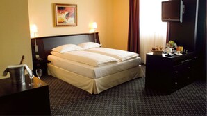 A hotel room with a bed, two bedside lamps, a television, a dresser, and a painting on the wall. - Hostellerie Du Chambellan (Pontpierre)