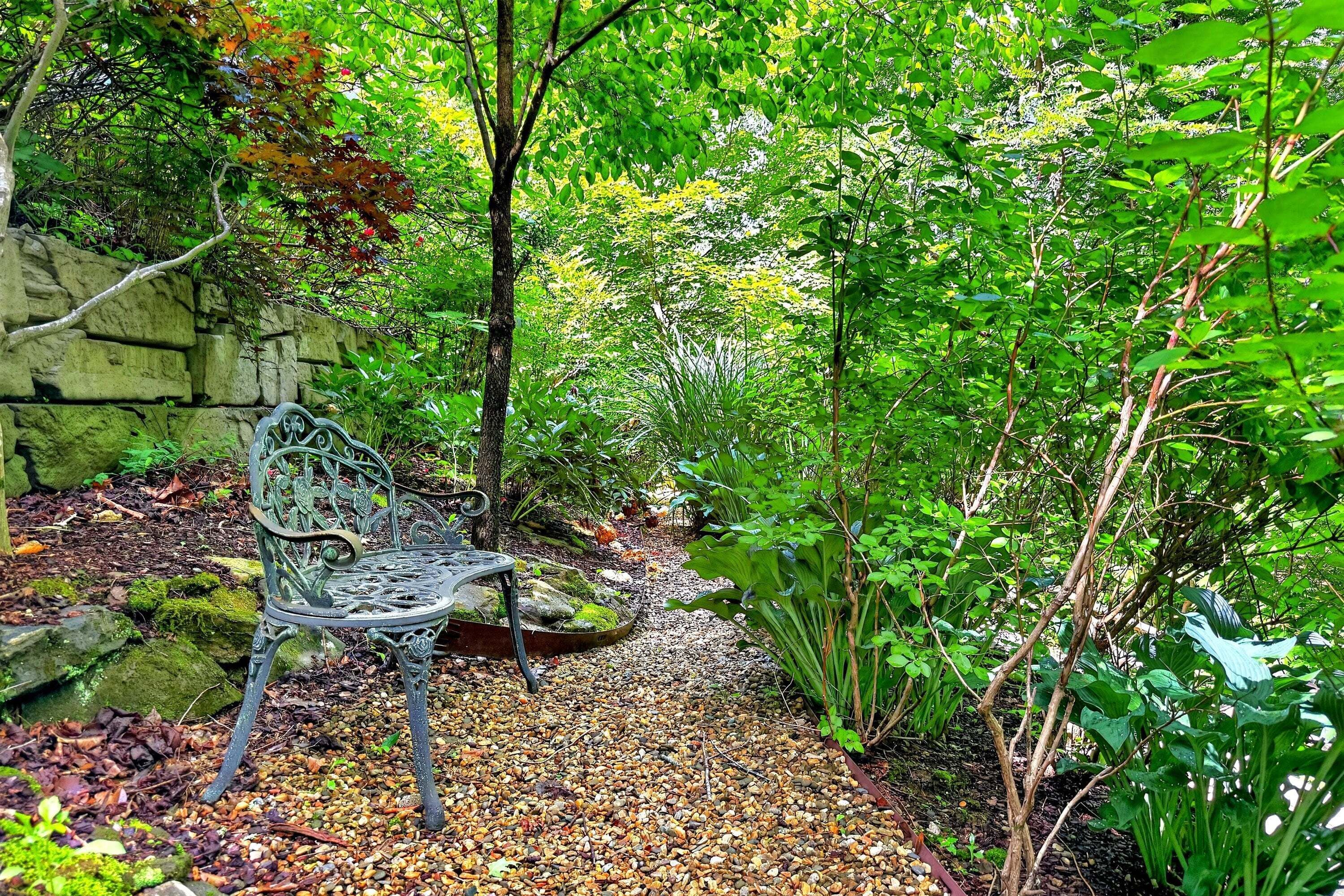 Un jardin avec un banc en métal, un mur en pierre et diverses plantes.
