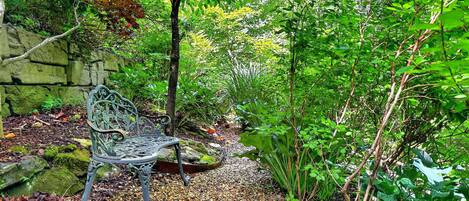 Un jardin avec un banc en métal, un mur en pierre et diverses plantes.