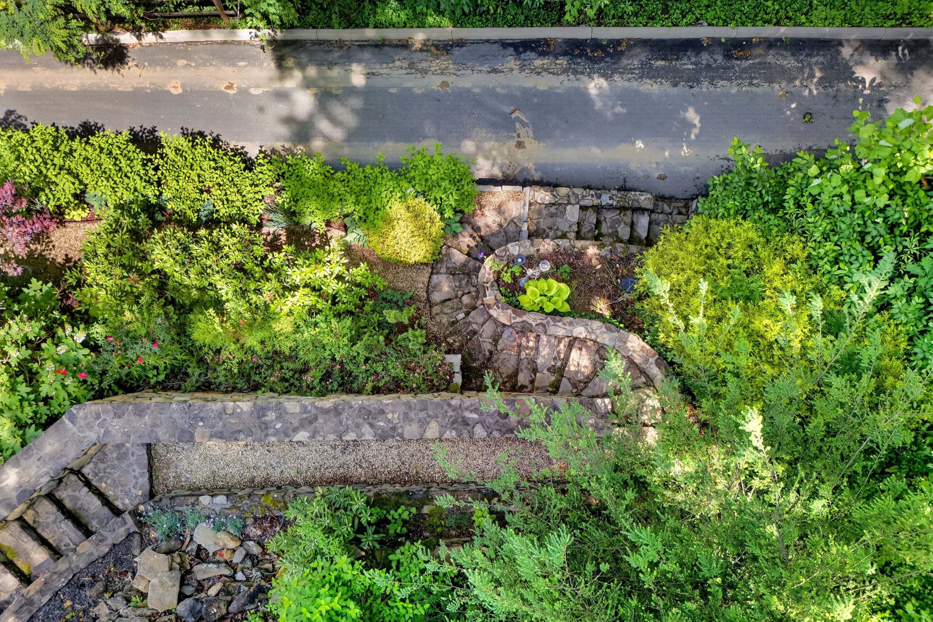 A stone retaining wall with a spiral design, surrounded by lush greenery and a road above.
