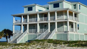 Una casa de varios pisos frente a la playa, con balcón, escaleras y vista al océano.