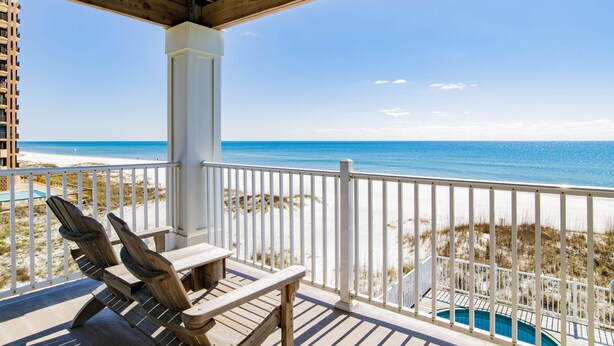 Una terraza de madera con dos sillas Adirondack, una piscina y vistas a la playa y al océano.