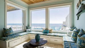 Una habitación con un amplio ventanal con vistas al océano, un banco empotrado con espacio de almacenamiento, una mesa redonda y un jarrón decorativo.