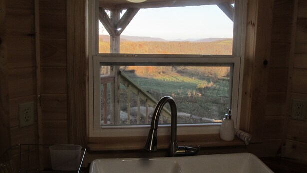 A rustic cabin interior with a wooden interior, a window overlooking a landscape, a sink, and a small countertop. - Lost Valley View Cabin (Ponca)