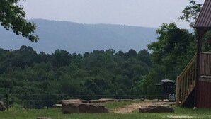 A wooden structure with a ramp, surrounded by a grassy field and large rocks. - Lost Valley View Cabin (Ponca)