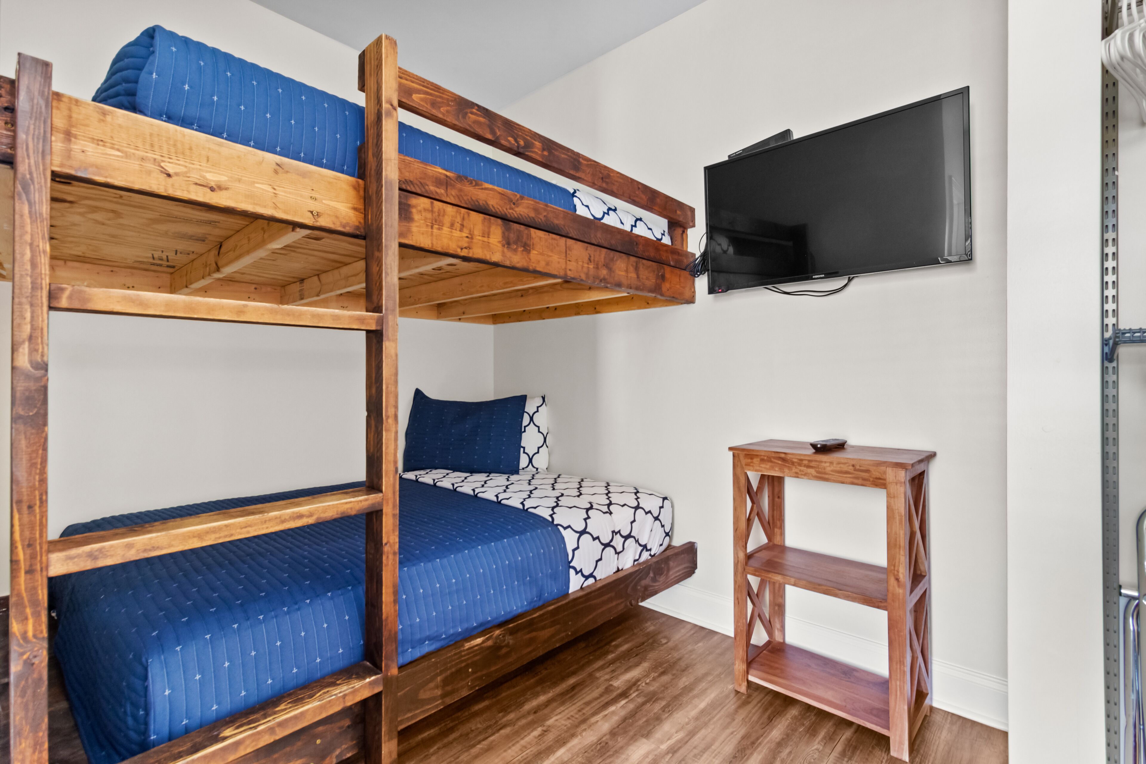 A bunk bed with a TV mounted on the wall above it, a wooden side table, and a shelf unit.