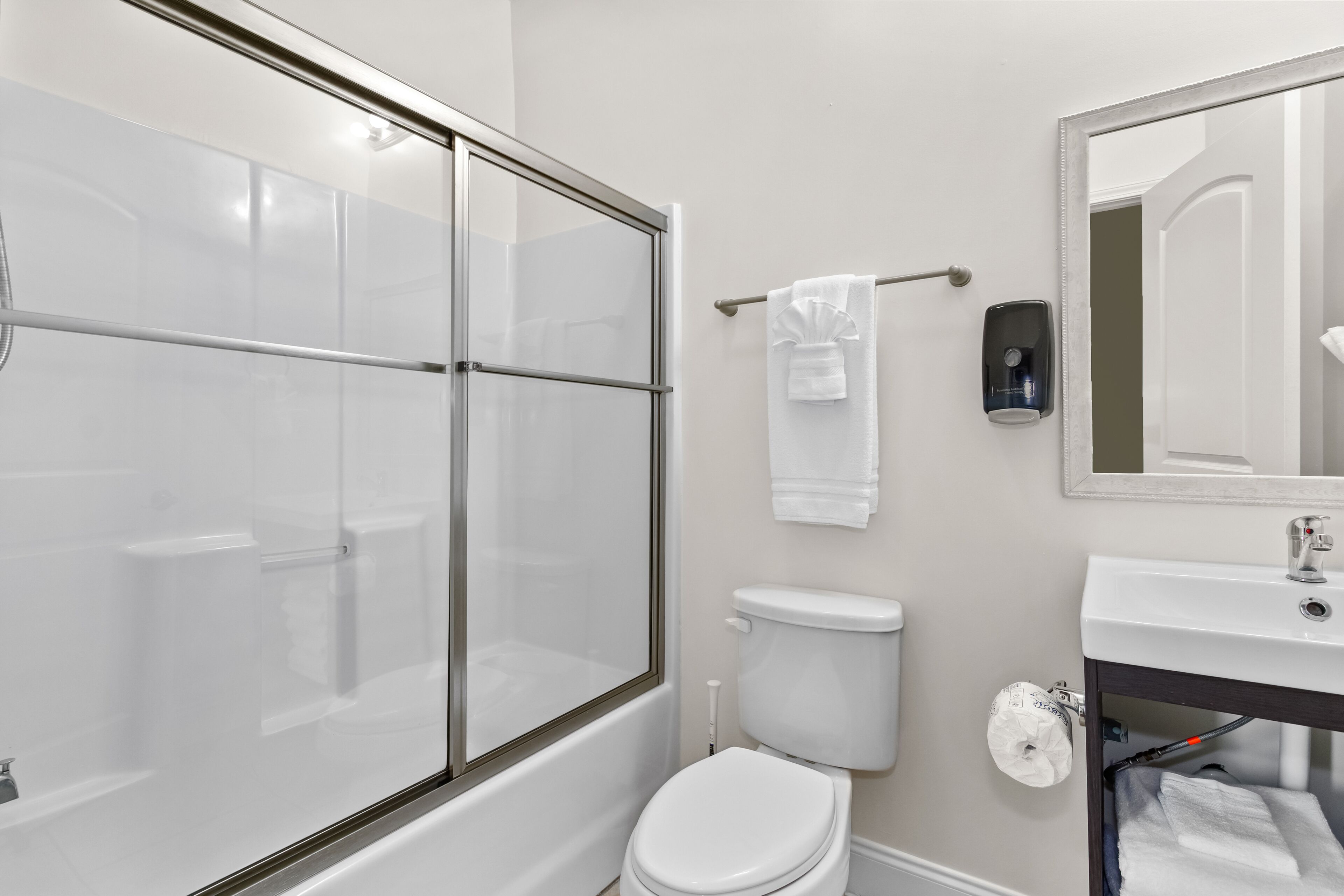 A modern bathroom with a glass-enclosed shower, a white toilet, and a sink with a mirror above it.