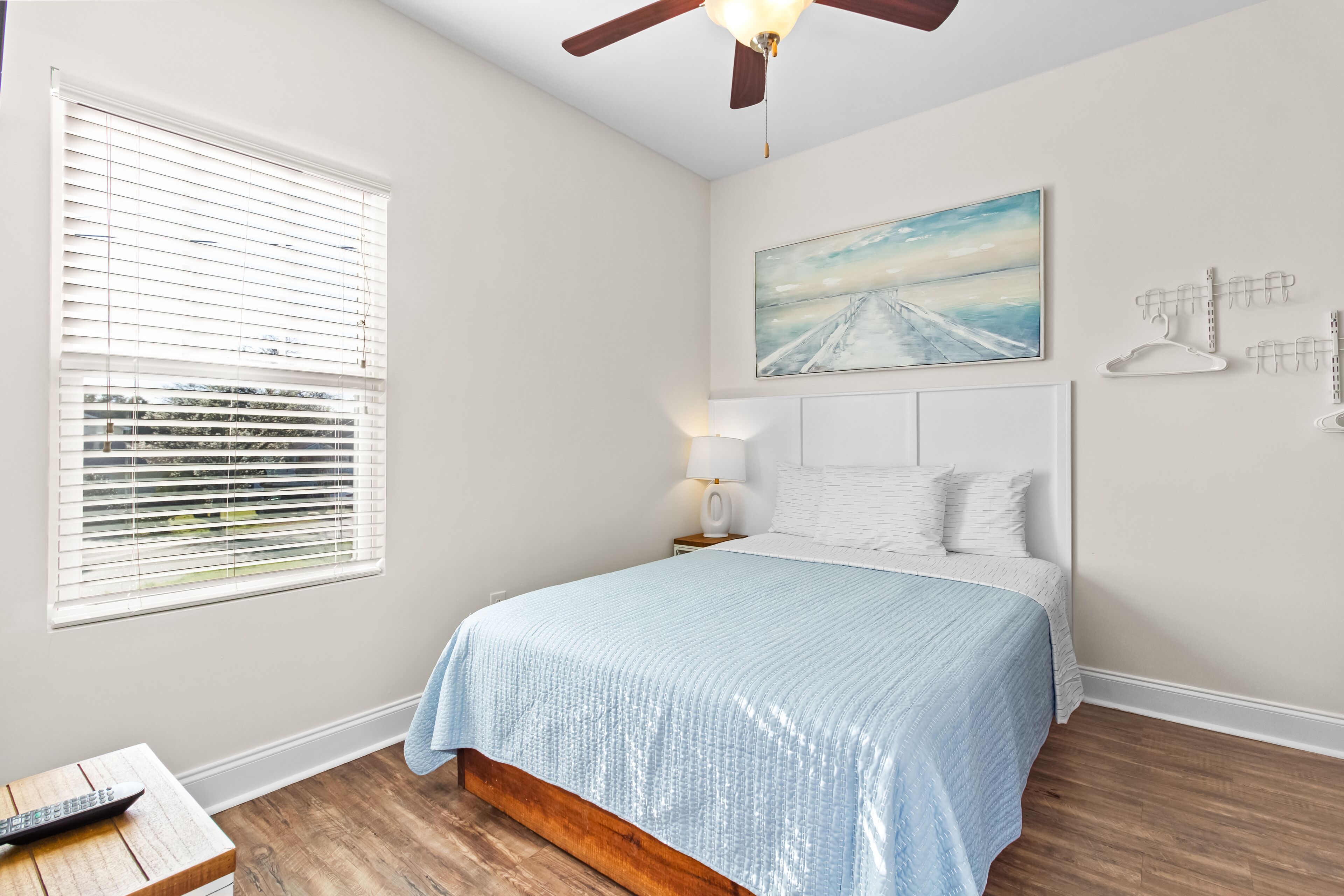 A bedroom with a bed, a ceiling fan, a painting, and a window with blinds.