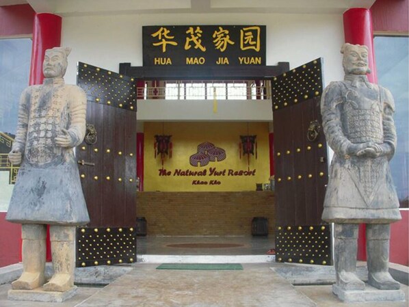 Une porte chinoise traditionnelle, flanquée de deux statues de lions en pierre de chaque côté, mène à un bâtiment sur lequel on peut lire l’inscription « HUA MAO JIA YUAN ».