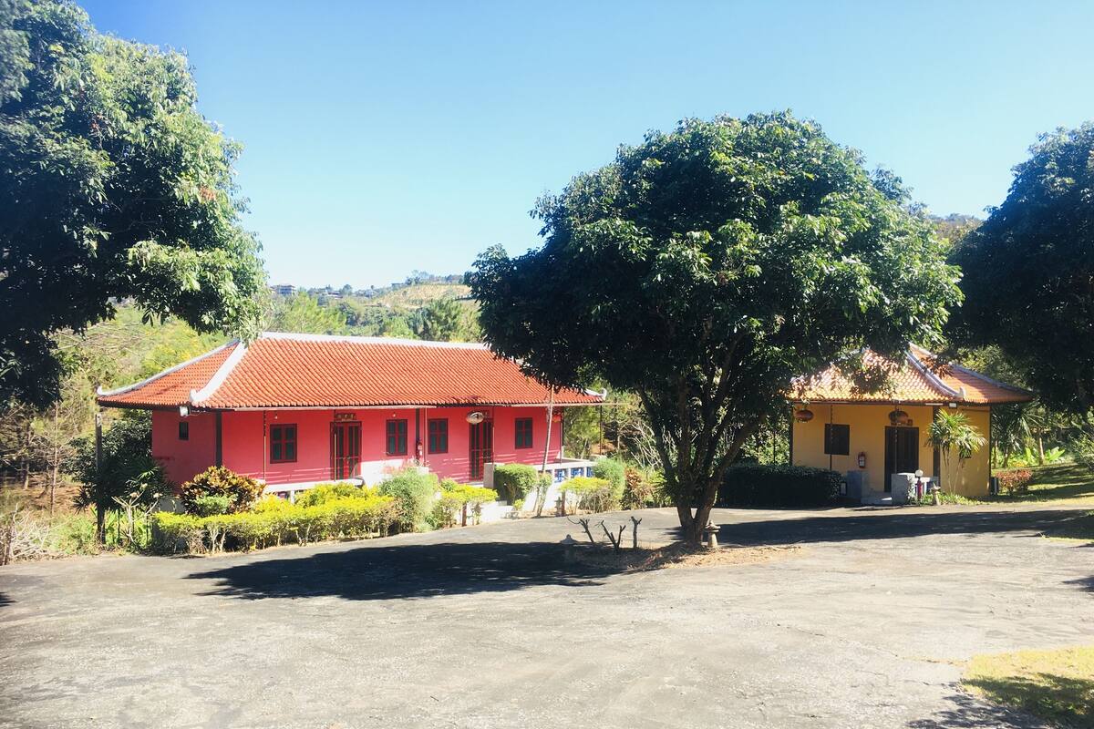 Un bâtiment rouge avec un toit en tuiles, un bâtiment jaune avec un toit en tuiles, et un grand arbre au premier plan.