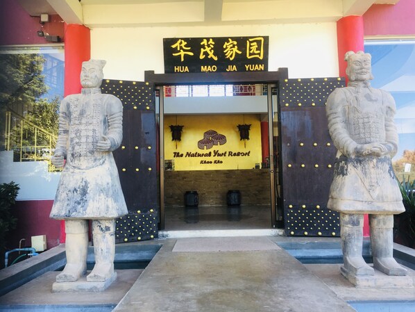 L’entrée d’un immeuble est ornée de deux statues en pierre, d’une enseigne indiquant « HUA MAO JIA YUAN » et d’une banderole pour « The Natural Yurt Resort ».