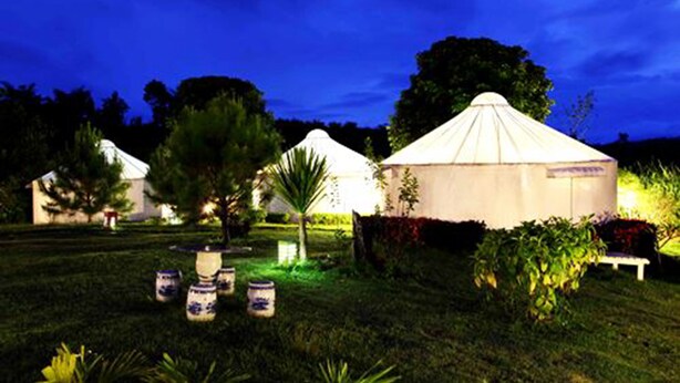 A yurt-style tent with a conical roof, surrounded by a well-maintained garden with potted plants and a bench. - The Natural Yurt Resort at Khao Kho (Khao Kho)