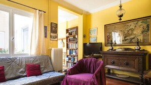 Una sala de estar con un sofá, un sillón púrpura, una estantería, un televisor y un cuadro en la pared.