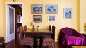 Un comedor con una mesa de madera, cuatro sillas y una butaca morada apoyada sobre ella. Cuatro cuadros enmarcados decoran la pared sobre la mesa.