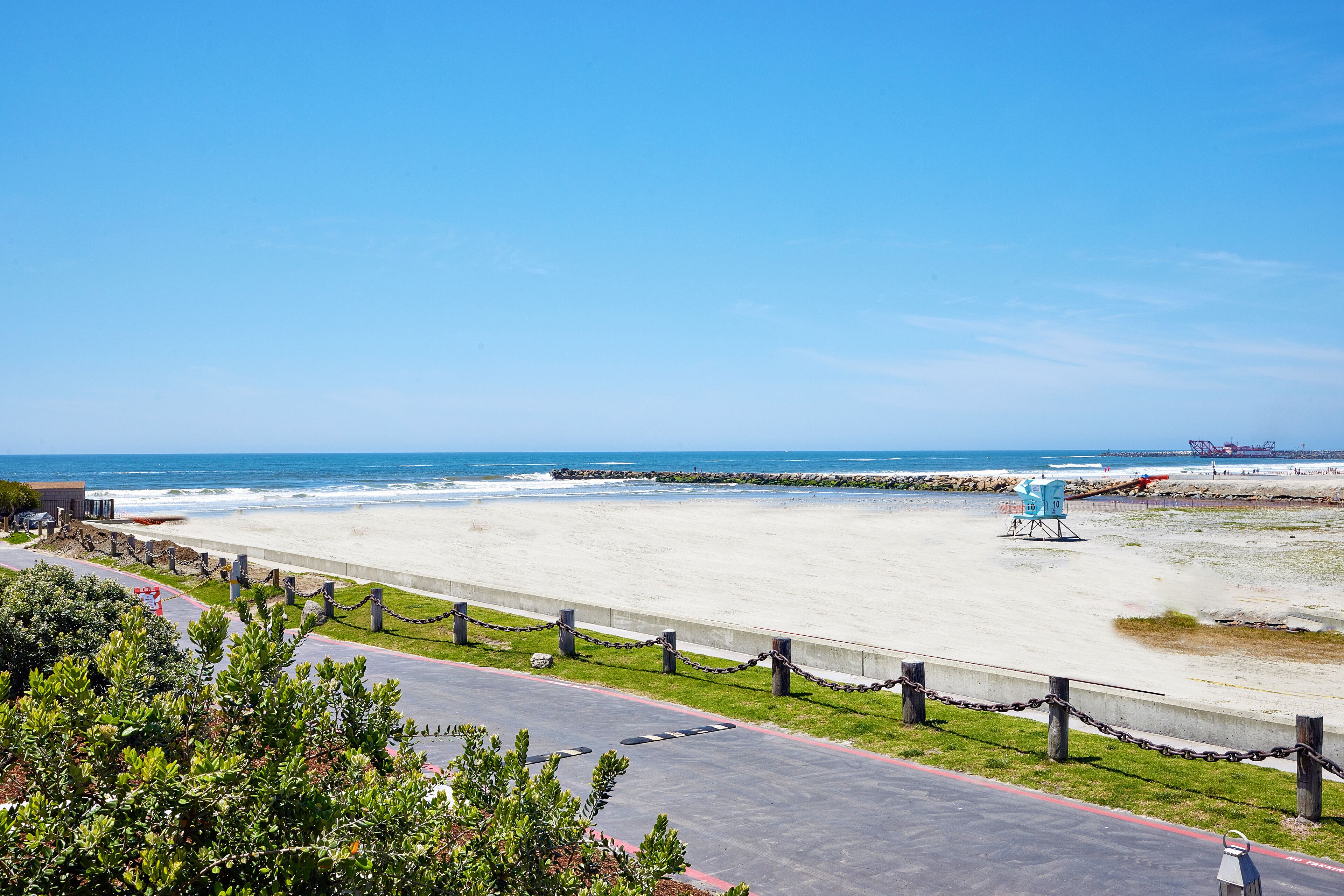 A beach with a lifeguard tower, a rocky breakwater, and a clear blue sky.