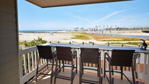 Ein Balkon mit drei Korbstühlen, Blick auf den Strand und einem klaren Himmel.