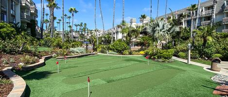 A golf course with a putting green surrounded by palm trees and a pool area.