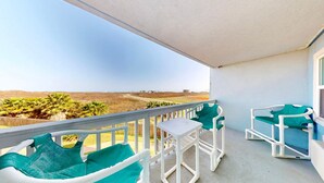 A balcony with white chairs and a table, overlooking a landscape with palm trees and a distant building. - Studio Condo in Town, Near Beach, Shared Pool and Hot Tub (Port Aransas)