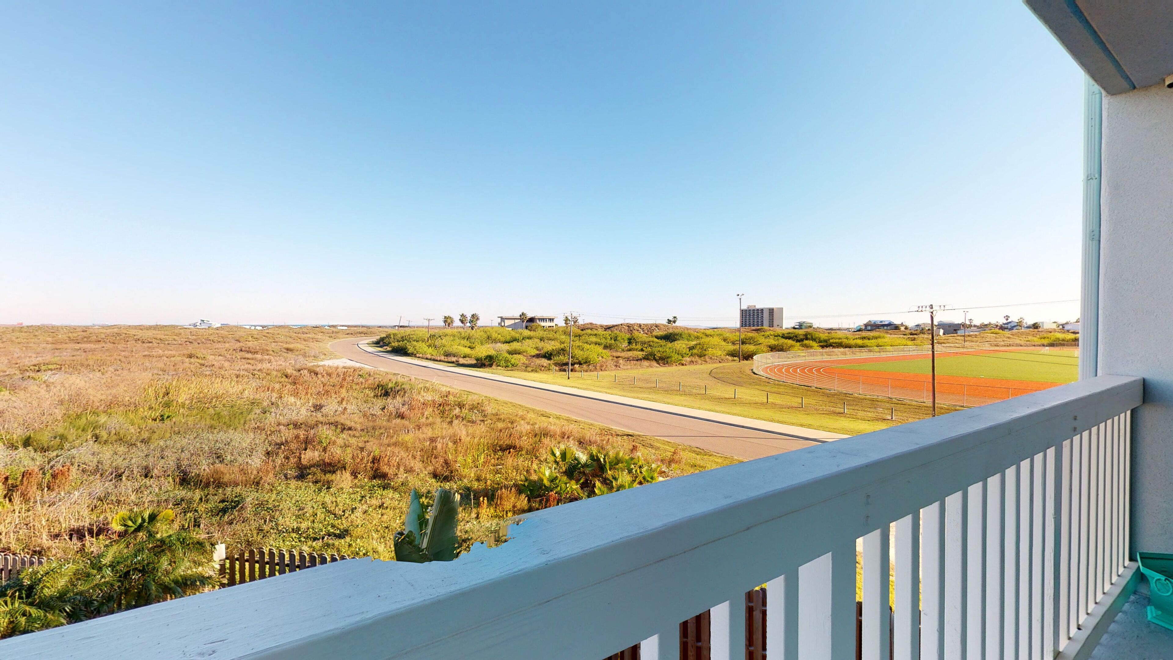 A view from a balcony overlooking a road, a green field, and a running track.