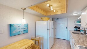 A compact kitchen with a white refrigerator, wooden ceiling, and a wall-mounted light fixture. - Studio Condo in Town, Near Beach, Shared Pool and Hot Tub (Port Aransas)
