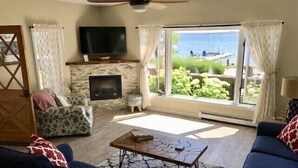 A living room with a fireplace, a television, and a view of the sea. - July 25th - Aug. 1st Available! (Charlevoix)