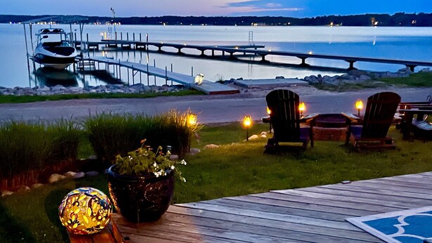 A deck with chairs and a potted plant, overlooking a body of water and a dock. - July 25th - Aug. 1st Available! (Charlevoix)