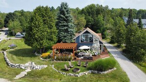 A two-story house with a stone facade, a covered patio with outdoor furniture, and a well-maintained garden with a stone pathway. - July 25th - Aug. 1st Available! (Charlevoix)