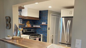 A modern kitchen with a wooden countertop, bar stools, a stainless steel refrigerator, and a blue tiled backsplash. - July 25th - Aug. 1st Available! (Charlevoix)