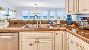 A kitchen with a stainless steel sink, white cabinets, and a view of the ocean.