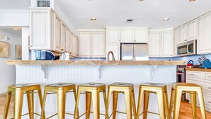A kitchen with white cabinetry, a stainless steel refrigerator, and a bar stool area.