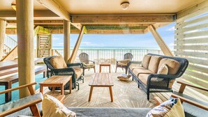A covered outdoor seating area with wicker furniture, a wooden table, and a view of the ocean.