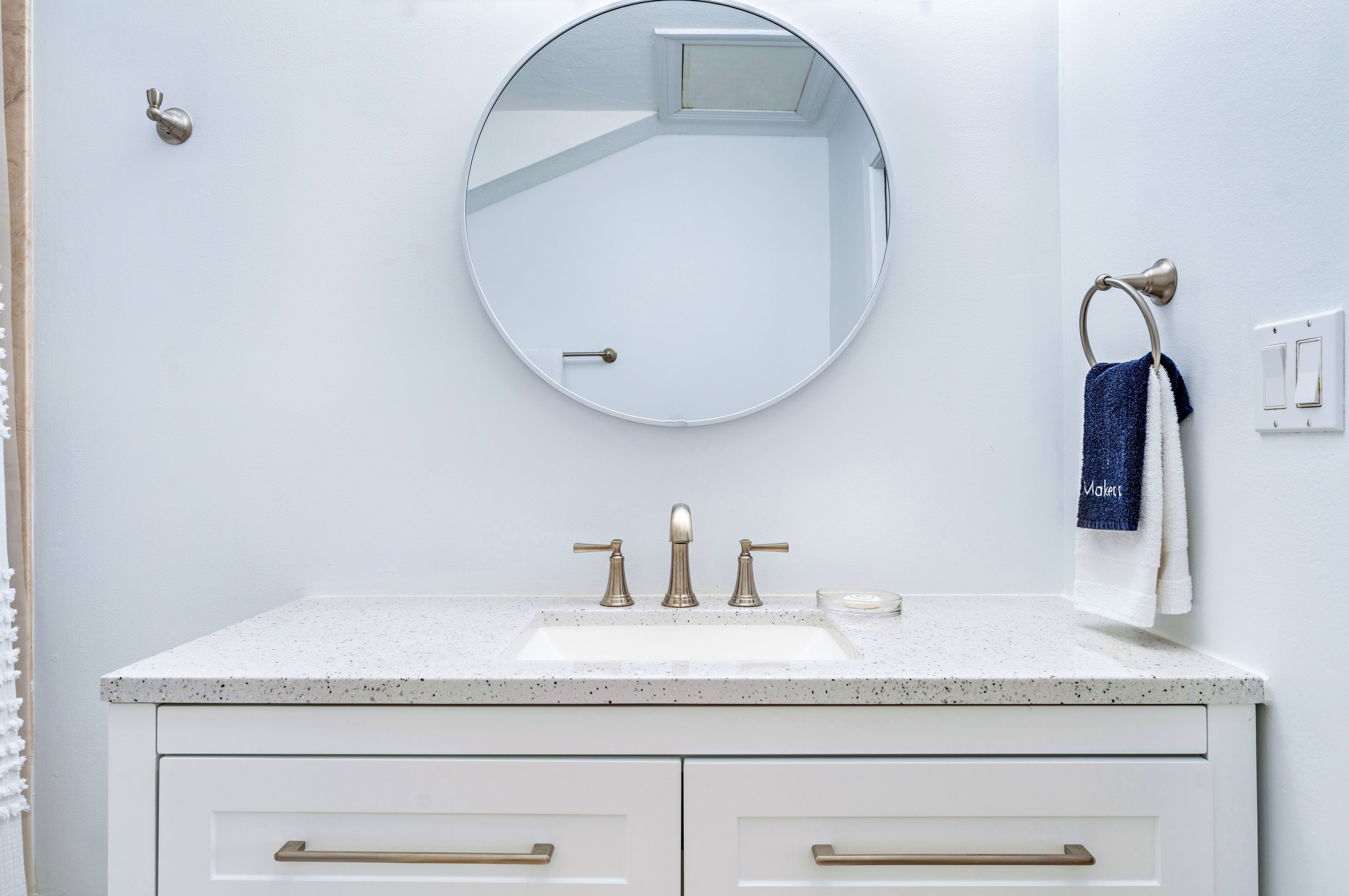 A bathroom with a white sink, two gold faucets, a round mirror, and a towel rack with a blue towel.