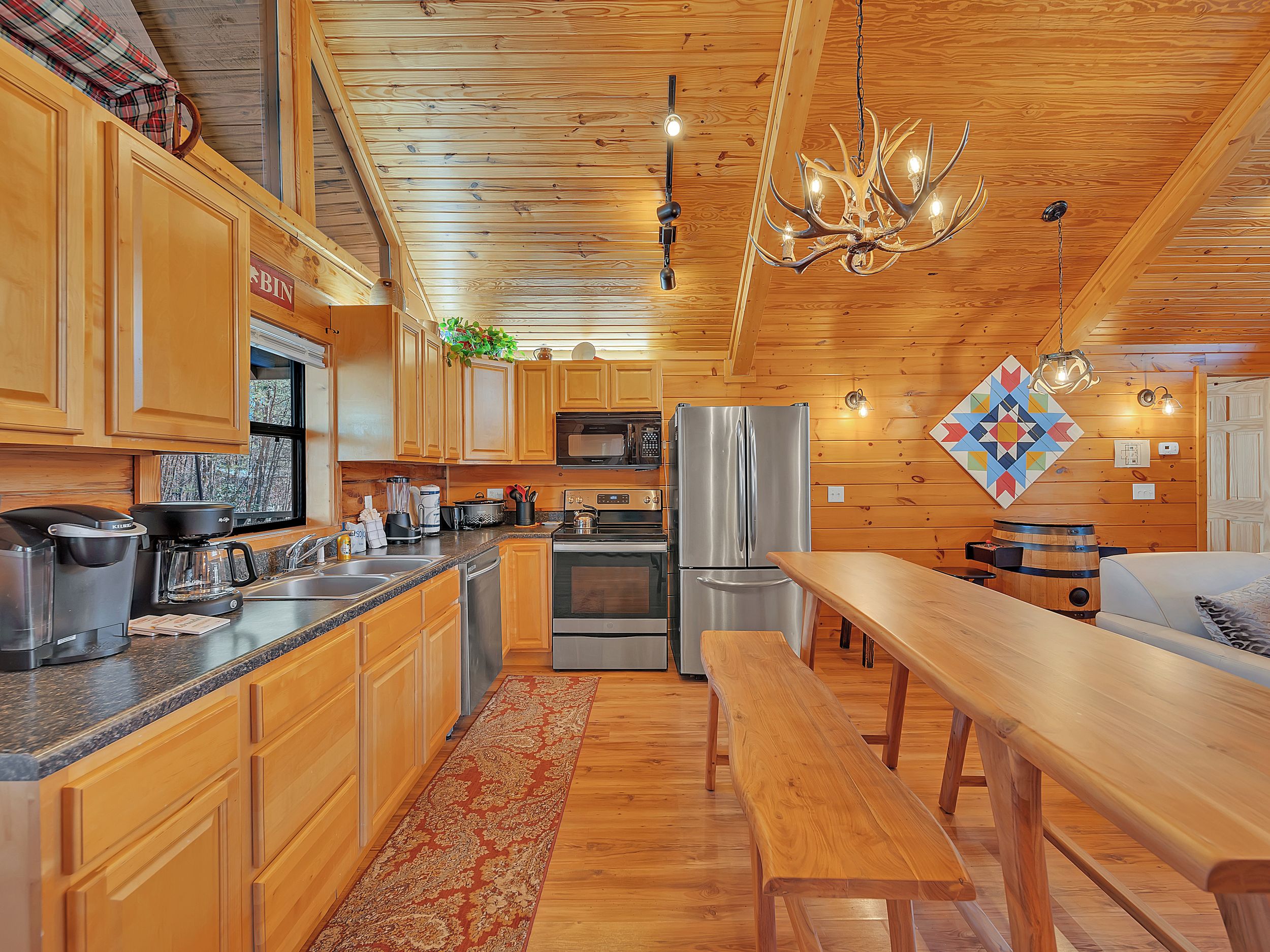 A modern kitchen with wooden cabinets, stainless steel appliances, a large island, and a chandelier.