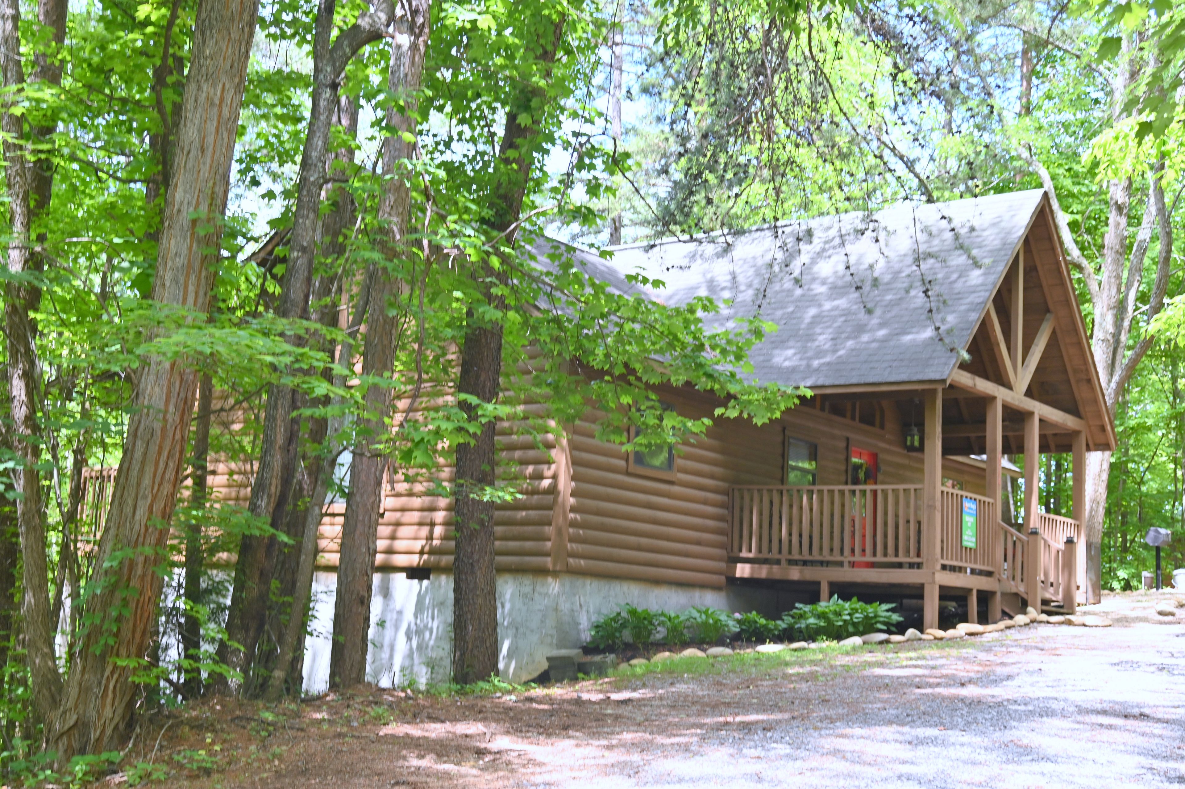 A wooden cabin with a porch, surrounded by trees.