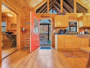 A wooden cabin with a red door, a kitchen with wooden cabinets, a sink, and a coffee maker.