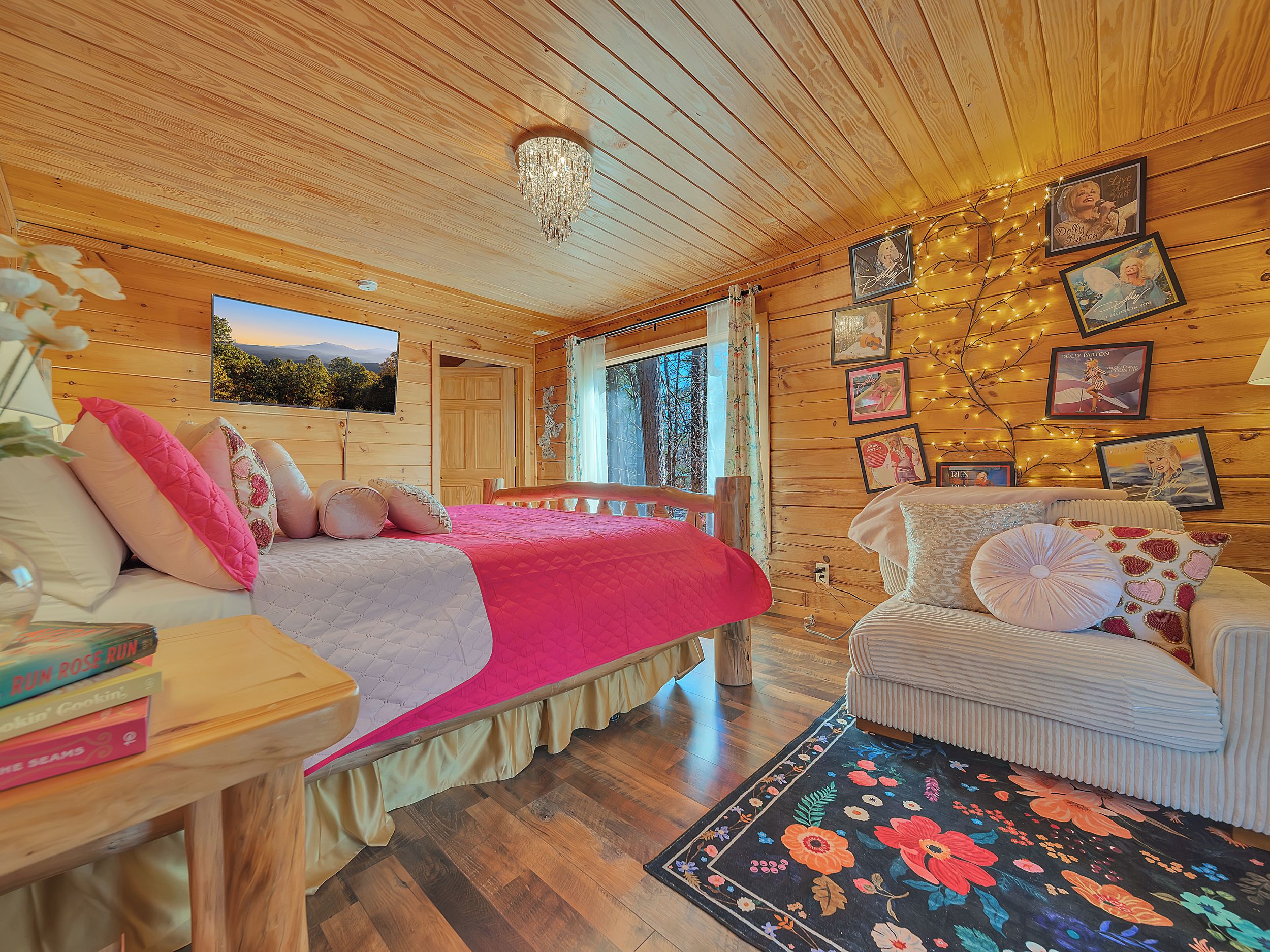Een gezellige houten kamer met een bed, een stoel en een vloerkleed. Er hangen fotolijstjes aan de muur en er is een raam met gordijnen.