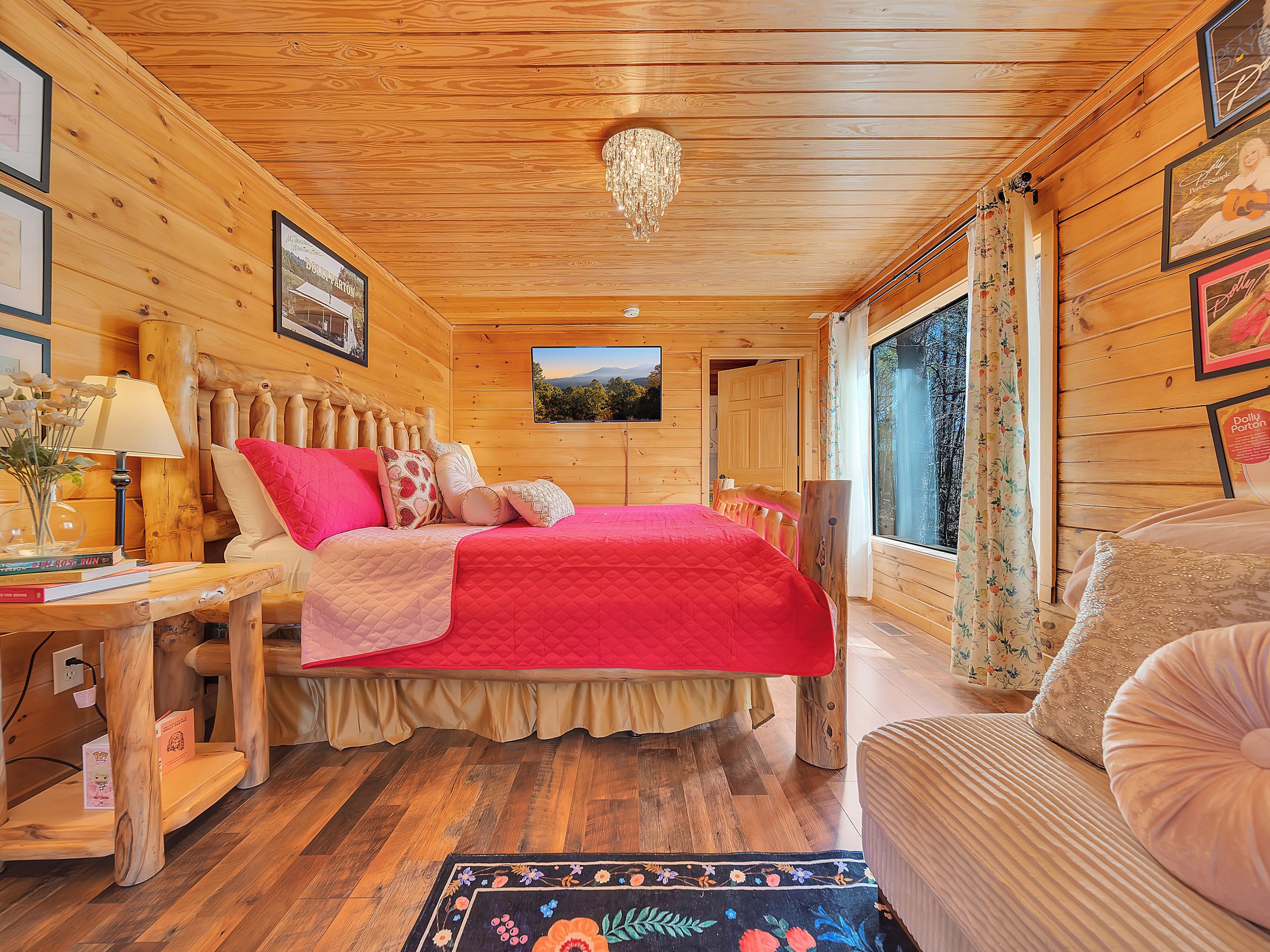 A wooden cabin bedroom with a bed, bedside table, lamp, and a large window.
