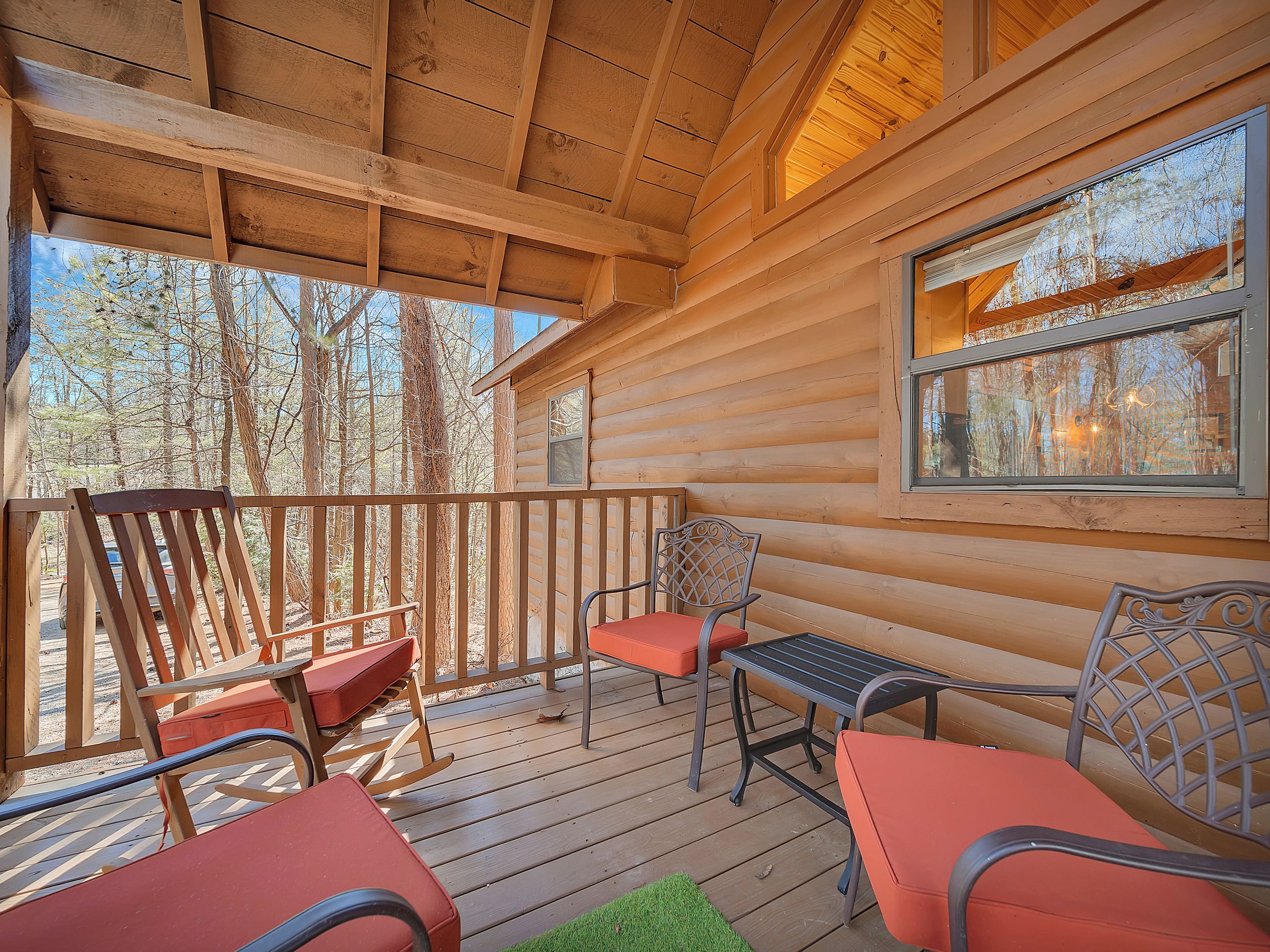 A wooden deck with outdoor seating, including chairs and a bench, overlooking a forested area.